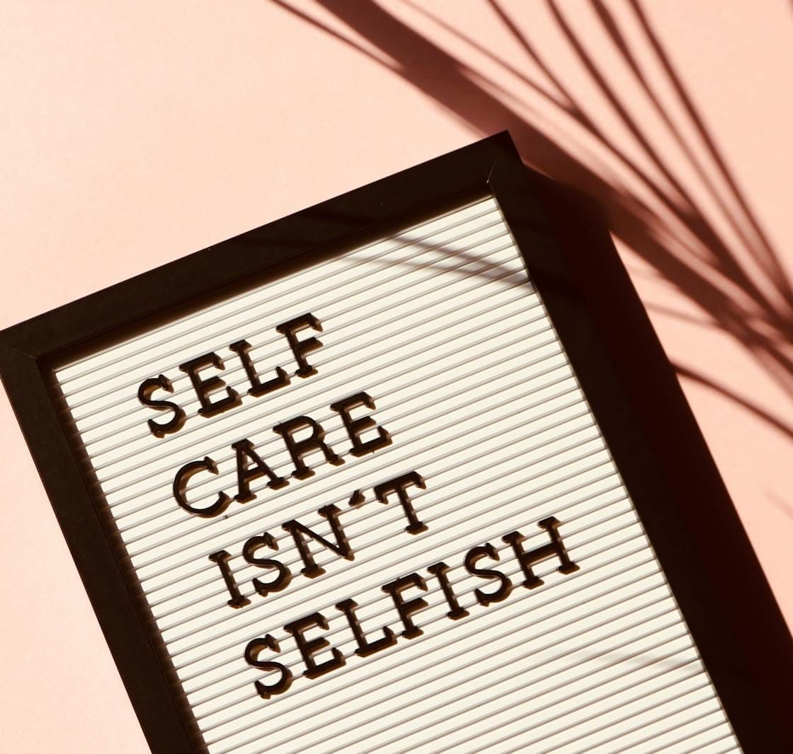Letter board displaying 'Self Care Isn't Selfish' with artistic shadow on pink background.