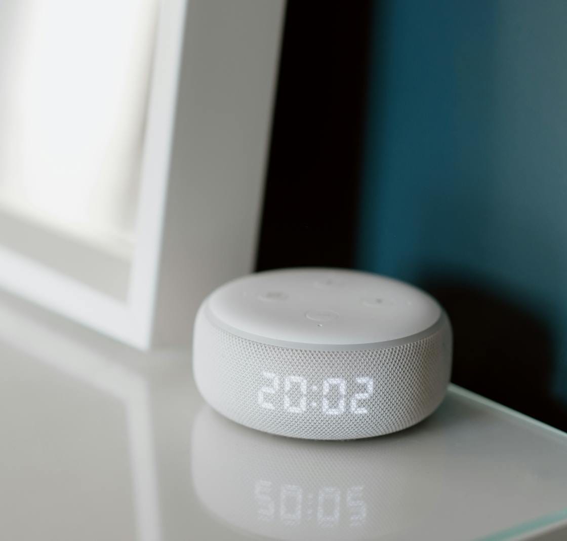 Close-up of a smart speaker with an illuminated 20:02 LED clock display on a desk.