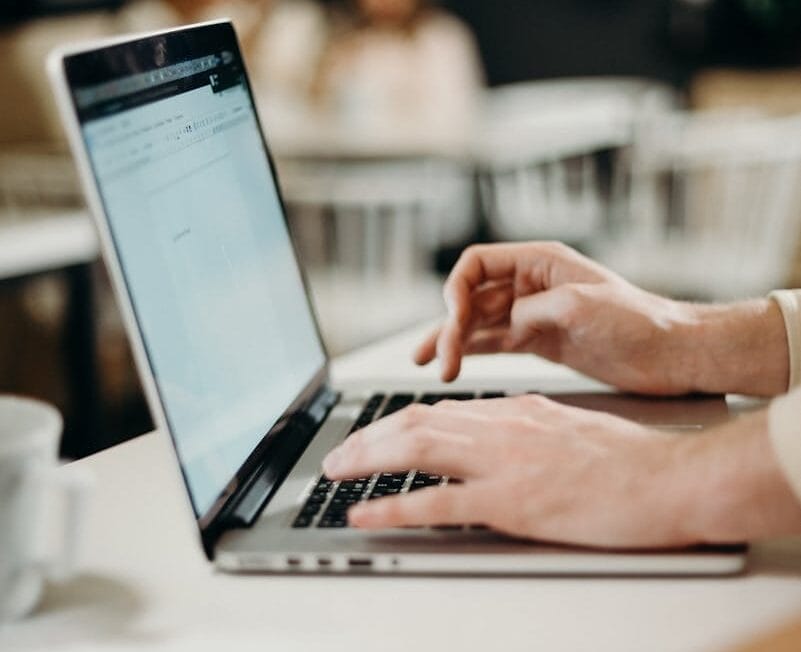 Close-up of hands typing on a laptop in a cozy indoor cafe setting.