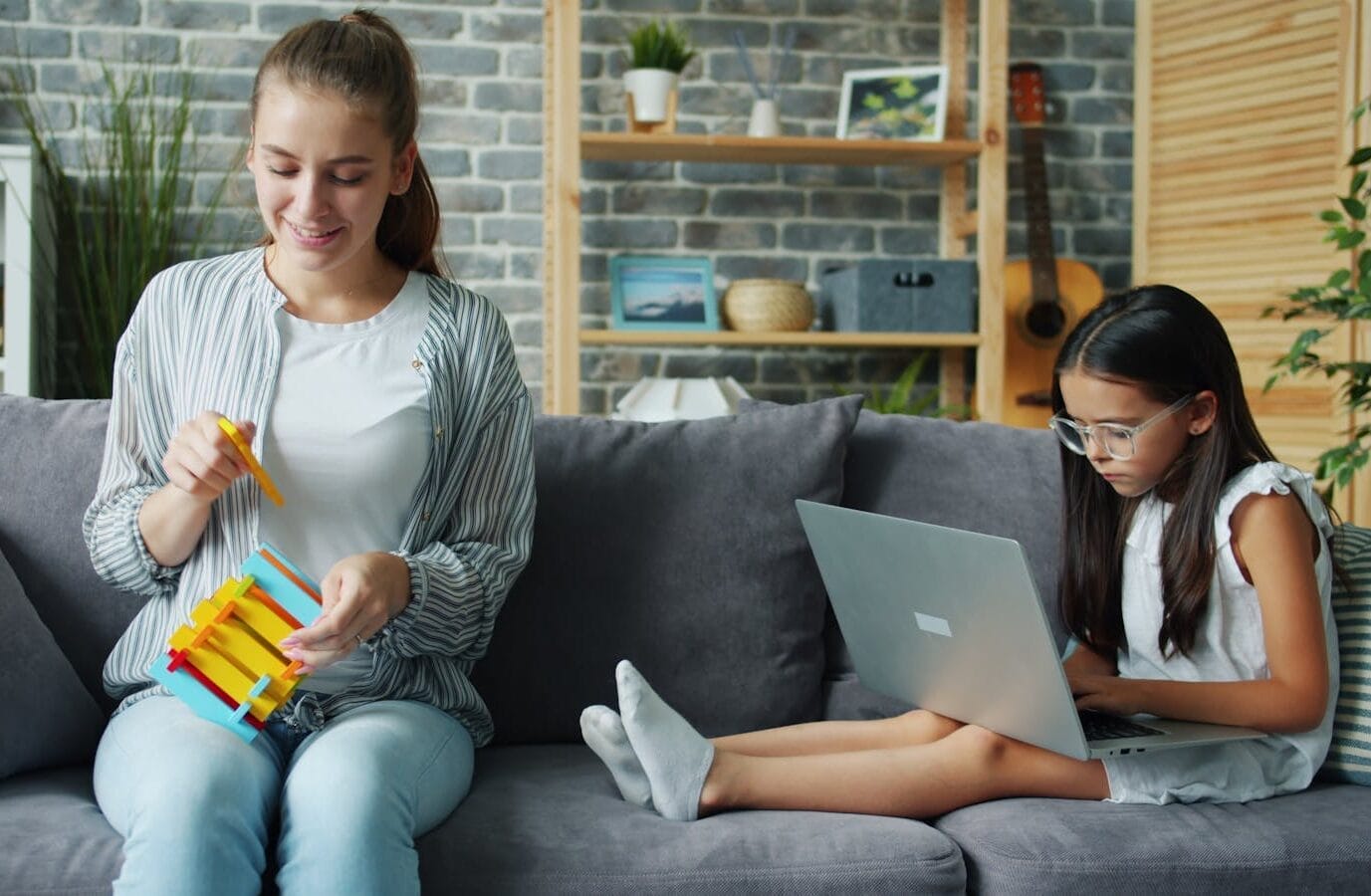 A woman plays a xylophone while a girl works on a laptop in a cozy living room.